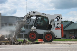 Kadlec Excavating Bobcat skidloader breaking highway concrete in front of FirstLight Health Center, Mora, MN. (close up)